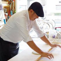 講師がこねた蕎麦粉を棒を使って伸ばす方法を実演する