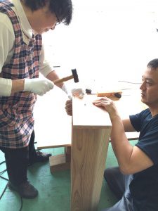 参加者の女性が金槌を使って箱に釘を打つ